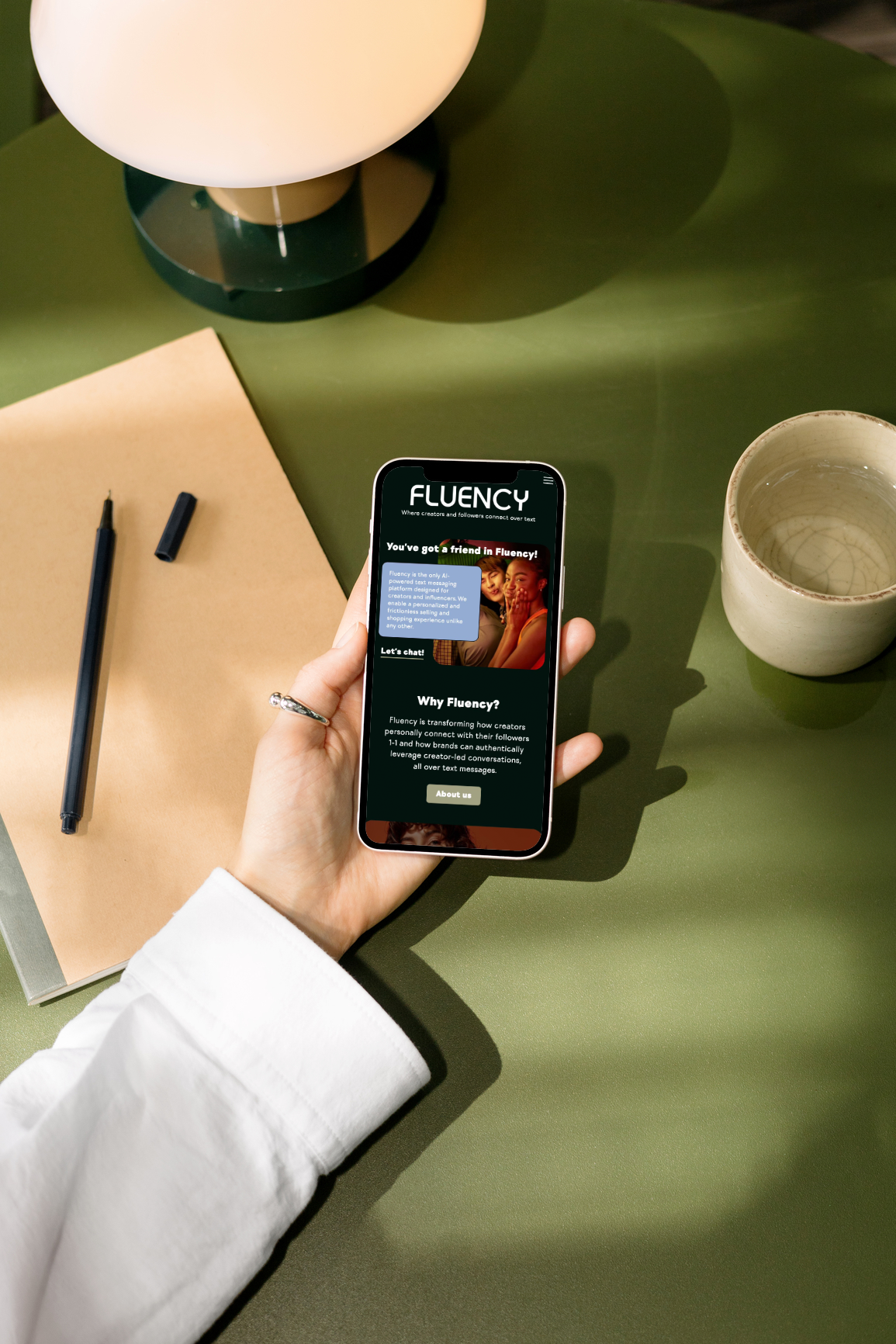 Woman's hand holding smartphone over desk with Fluency website